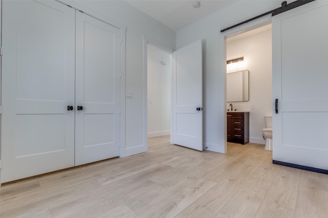 unfurnished bedroom with light wood finished floors, connected bathroom, baseboards, a barn door, and a closet