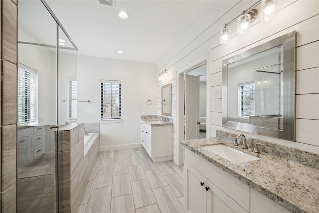 bathroom featuring a sink, visible vents, a garden tub, and two vanities