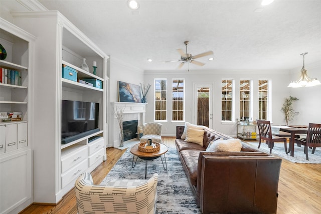 living area with crown molding, recessed lighting, light wood-style floors, a high end fireplace, and ceiling fan with notable chandelier