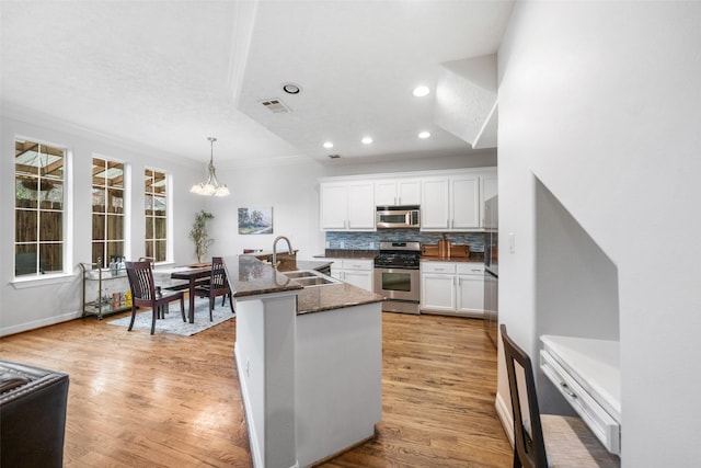 kitchen featuring appliances with stainless steel finishes, light wood-type flooring, white cabinetry, pendant lighting, and a sink