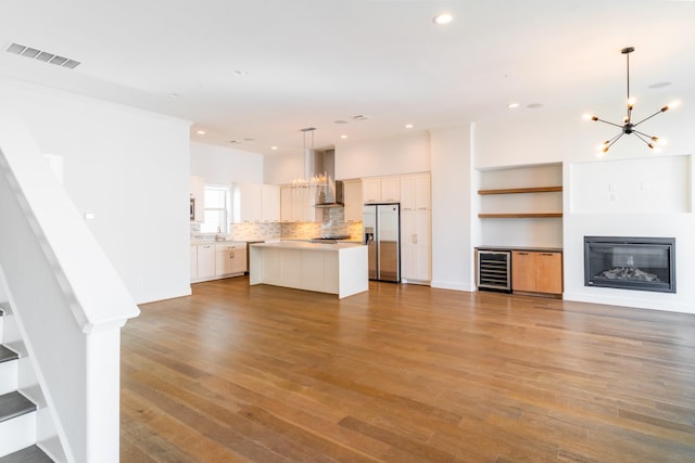 unfurnished living room with wine cooler, visible vents, an inviting chandelier, a glass covered fireplace, and wood finished floors