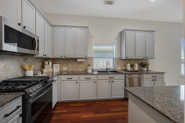 kitchen featuring visible vents, appliances with stainless steel finishes, dark wood-type flooring, a sink, and dark stone counters