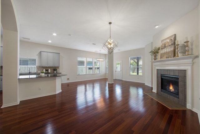 unfurnished living room with dark wood-type flooring, a tile fireplace, baseboards, and an inviting chandelier