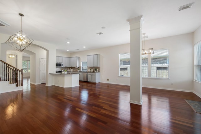 unfurnished living room with an inviting chandelier, plenty of natural light, baseboards, and dark wood finished floors