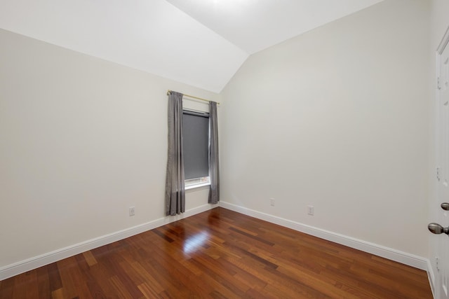 empty room featuring vaulted ceiling, dark wood finished floors, and baseboards