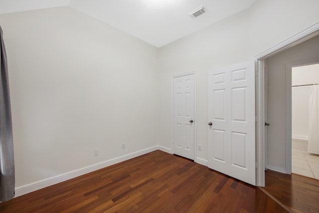 unfurnished bedroom featuring vaulted ceiling, dark wood finished floors, visible vents, and baseboards