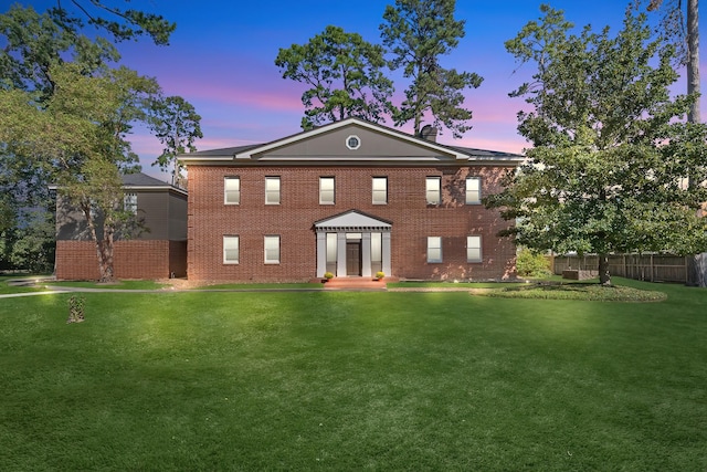 exterior space featuring brick siding, a lawn, and fence