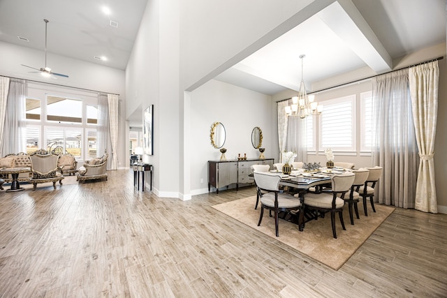 dining space featuring light wood-style flooring, a high ceiling, beamed ceiling, baseboards, and ceiling fan with notable chandelier