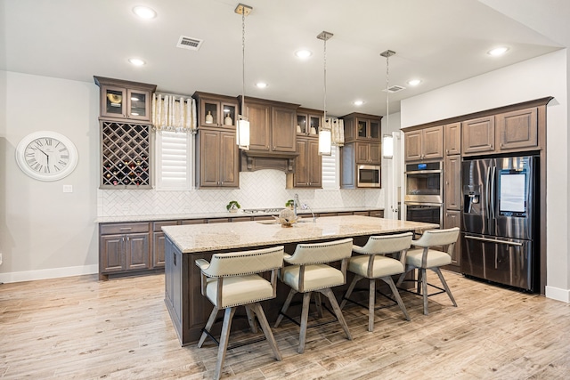 kitchen featuring visible vents, an island with sink, glass insert cabinets, light stone countertops, and stainless steel appliances