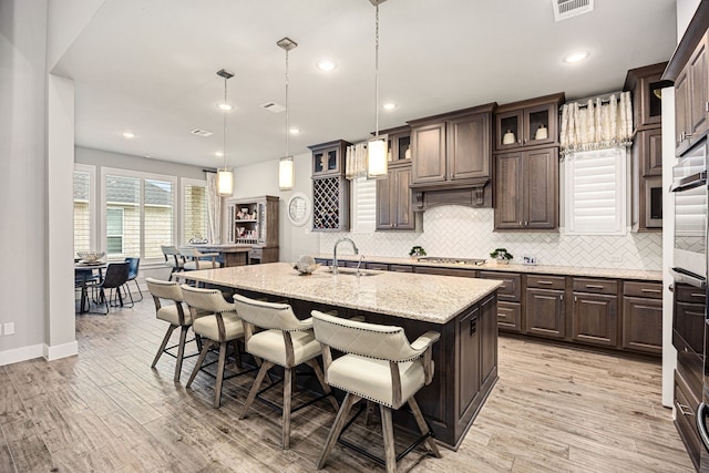 kitchen featuring an island with sink, a kitchen breakfast bar, dark brown cabinets, pendant lighting, and a sink