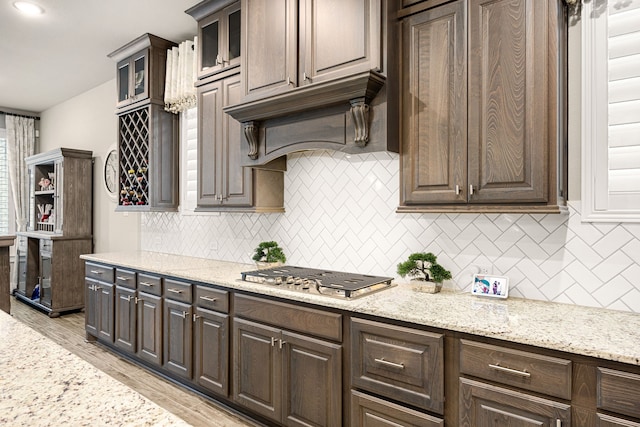 kitchen featuring glass insert cabinets, dark brown cabinetry, stainless steel gas stovetop, and custom exhaust hood