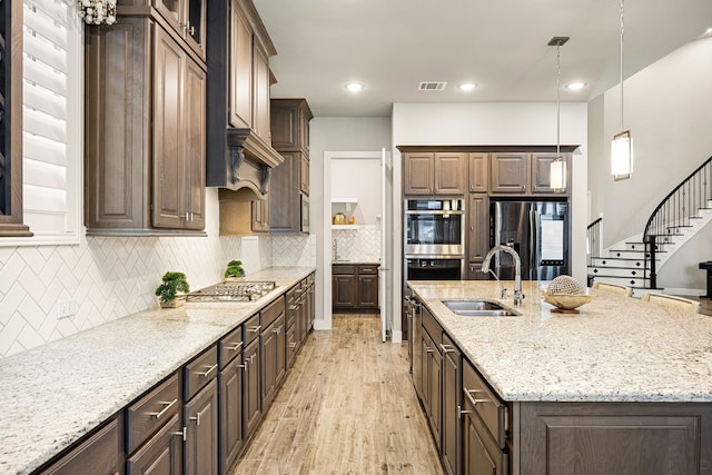 kitchen with appliances with stainless steel finishes, decorative light fixtures, a sink, and light stone countertops