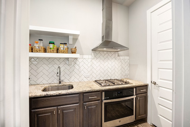 kitchen with wall chimney exhaust hood, stainless steel appliances, dark brown cabinets, open shelves, and a sink