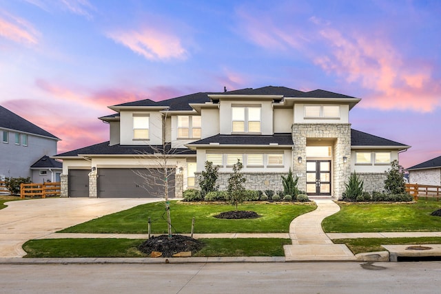 prairie-style home with stucco siding, concrete driveway, an attached garage, fence, and stone siding