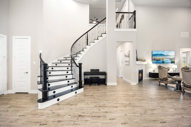 entryway with a towering ceiling, a warm lit fireplace, stairway, and light wood finished floors