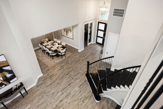 entryway with a towering ceiling, an inviting chandelier, visible vents, and wood finished floors