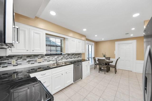 kitchen featuring dark countertops, appliances with stainless steel finishes, white cabinets, a sink, and light tile patterned flooring