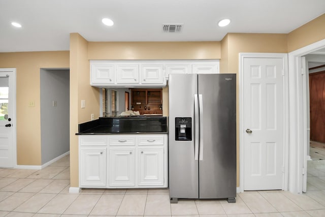 kitchen featuring visible vents, light tile patterned floors, stainless steel fridge, and white cabinetry