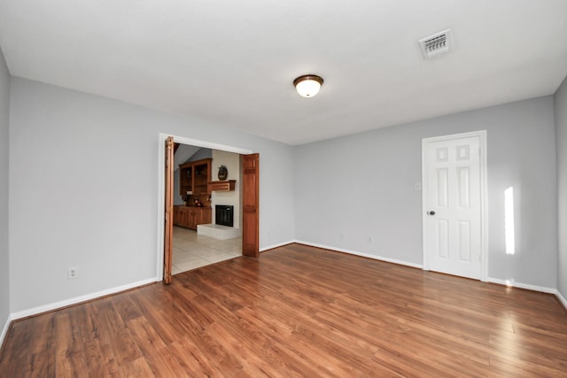 empty room with visible vents, a fireplace with raised hearth, baseboards, and wood finished floors