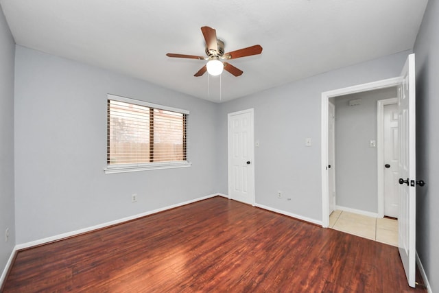 empty room with wood finished floors, a ceiling fan, and baseboards