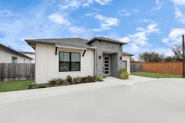 view of front of home with a garage, stone siding, roof with shingles, and fence