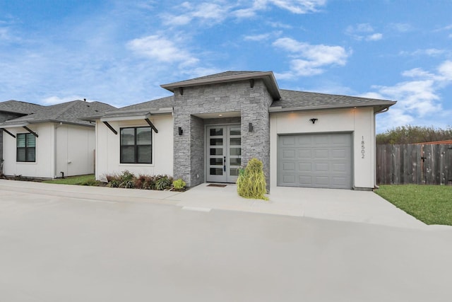 prairie-style home with a garage, fence, stone siding, concrete driveway, and roof with shingles