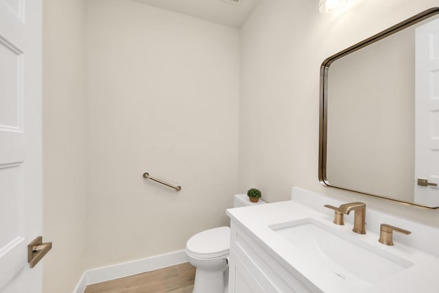 half bath featuring baseboards, vanity, toilet, and wood finished floors