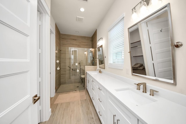 full bathroom featuring double vanity, visible vents, wood finished floors, a shower stall, and a sink