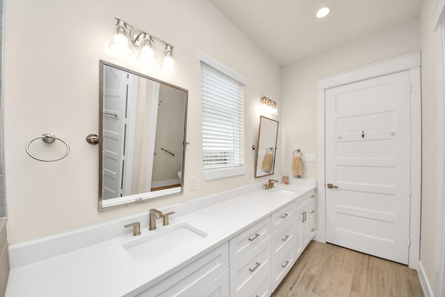 bathroom with recessed lighting, double vanity, a sink, and wood finished floors