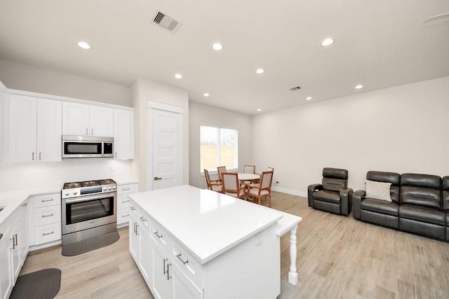 kitchen with visible vents, white cabinets, a kitchen island, stainless steel appliances, and light countertops