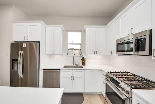 kitchen featuring stainless steel appliances, light countertops, backsplash, white cabinets, and a sink