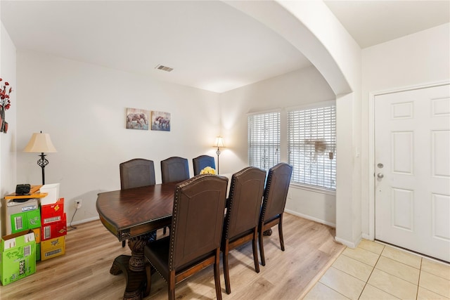 dining space with light wood-style floors, visible vents, arched walkways, and baseboards