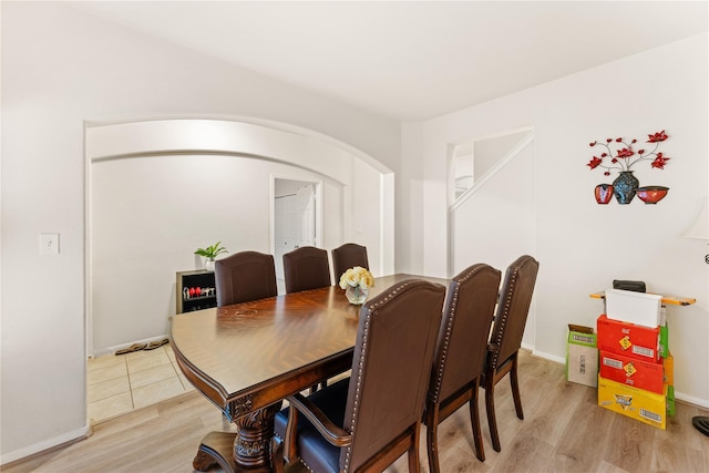 dining room with arched walkways, baseboards, and light wood-style floors