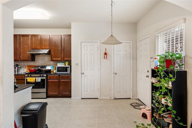 kitchen with tasteful backsplash, dark countertops, hanging light fixtures, stainless steel appliances, and under cabinet range hood