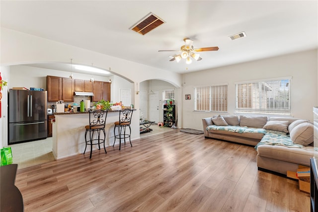 living area with a ceiling fan, arched walkways, visible vents, and light wood finished floors