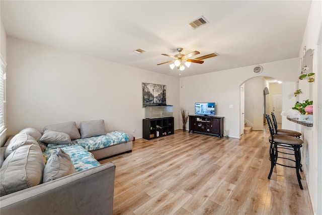 living room featuring light wood-style floors, arched walkways, visible vents, and stairway