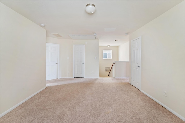 unfurnished room with attic access, light colored carpet, and baseboards