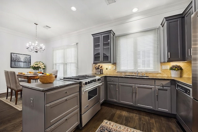 kitchen featuring stainless steel appliances, a sink, gray cabinets, dark countertops, and decorative light fixtures