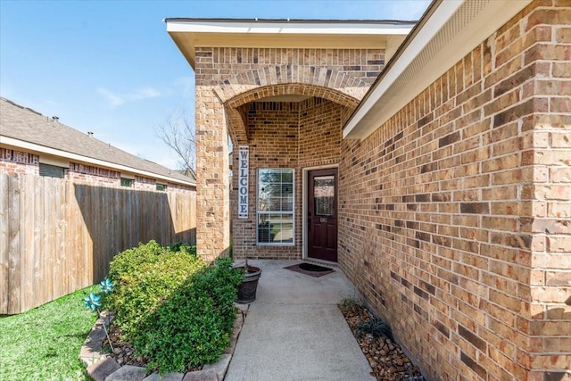 doorway to property with brick siding and fence