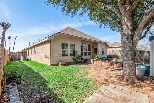 rear view of property featuring a yard, brick siding, a fenced backyard, and central air condition unit