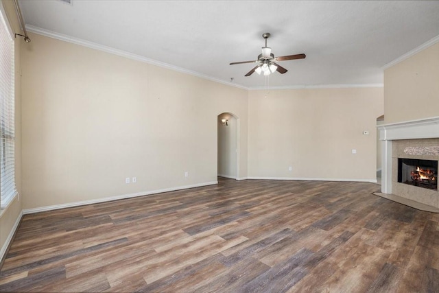 unfurnished living room with arched walkways, ceiling fan, dark wood-style flooring, and a tiled fireplace