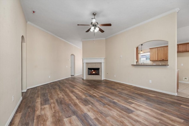 unfurnished living room featuring dark wood-style floors, ceiling fan, ornamental molding, and a fireplace