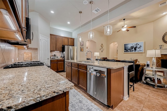 kitchen featuring light stone counters, arched walkways, a center island with sink, appliances with stainless steel finishes, and a sink