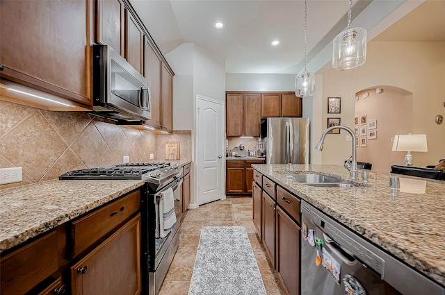 kitchen with stainless steel appliances, light stone counters, a sink, and decorative light fixtures