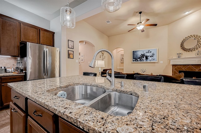 kitchen featuring freestanding refrigerator, a sink, decorative backsplash, and light stone countertops