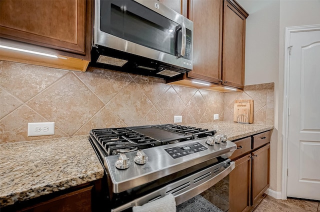 kitchen with brown cabinets, light stone countertops, stainless steel appliances, and decorative backsplash