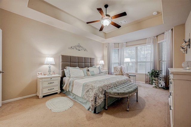 bedroom with light colored carpet, a ceiling fan, baseboards, visible vents, and a tray ceiling