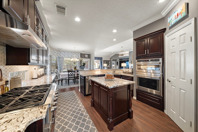 kitchen with a peninsula, stainless steel appliances, a kitchen island, visible vents, and dark wood finished floors