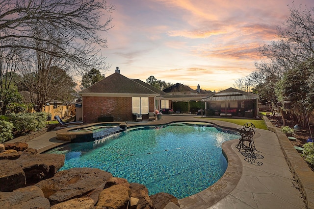 pool at dusk featuring a pool with connected hot tub, a patio, and a gazebo