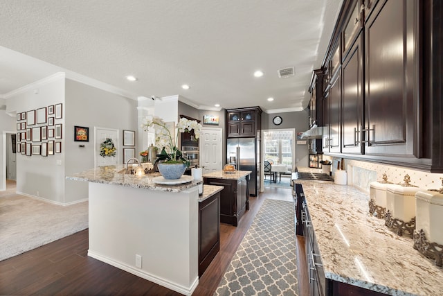 kitchen with an island with sink, appliances with stainless steel finishes, visible vents, and light stone counters